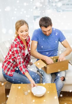 repair, moving in and people concept - smiling couple opening , unpacking cardboard box with dishes at home