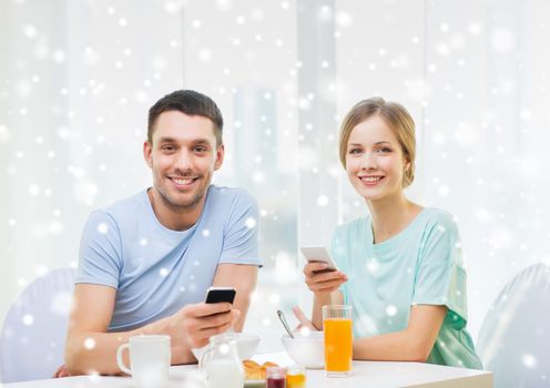 food, family, people and technology concept - smiling couple with smartphones and having breakfast at home