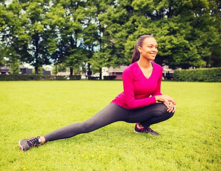 fitness, sport, training, park and lifestyle concept - smiling african american woman stretching leg outdoors