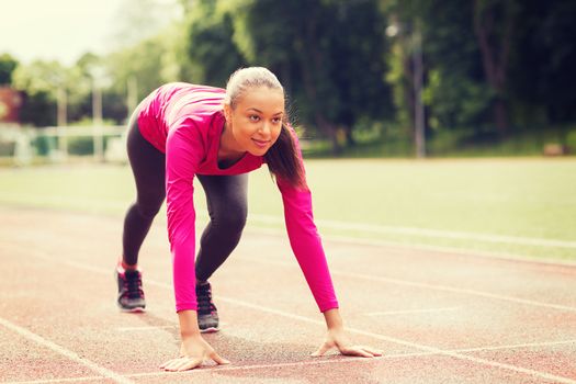 fitness, sport, training and lifestyle concept - smiling african american woman running on track outdoors