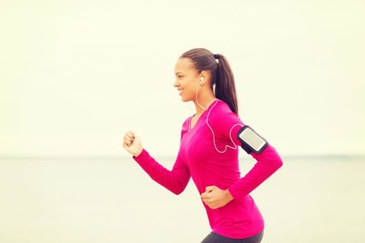 sport, fitness, health, technology and people concept - smiling young african american woman running with smartphone and earphones outdoors