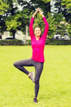 sport, exercise, park and lifestyle concept - smiling african american woman exercising outdoors