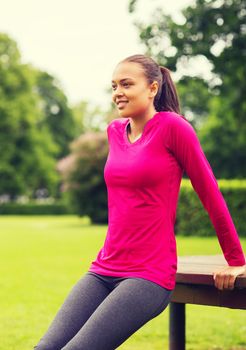 fitness, sport, training, park and lifestyle concept - smiling african american woman doing push-ups on bench outdoors