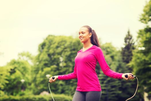 fitness, sport, training, park and lifestyle concept - smiling african american woman exercising with jump-rope outdoors