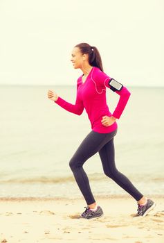 sport, fitness, health, technology and people concept - smiling young african american woman running with smartphone and earphones outdoors