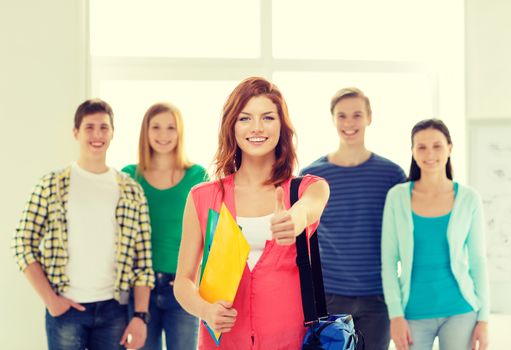 education and school concept - group of smiling students with teenage girl in front with bag and folders showing thumbs up