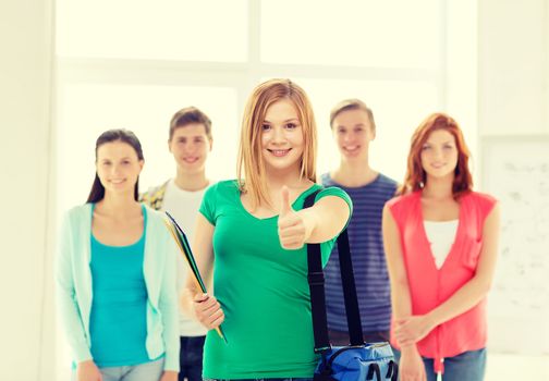 education and school concept - group of smiling students with teenage girl in front with bag and folders showing thumbs up