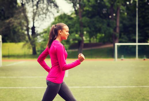 fitness, sport, training and lifestyle concept - smiling african american woman running on track outdoors