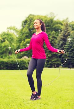 fitness, sport, training, park and lifestyle concept - smiling african american woman exercising with jump-rope outdoors