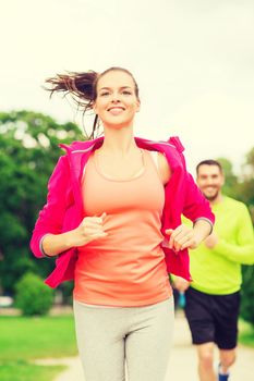 fitness, sport, friendship and lifestyle concept - smiling couple running outdoors