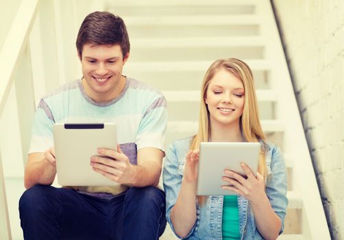 education and technology concept - smiling students with tablet pc computer sitting on staircase