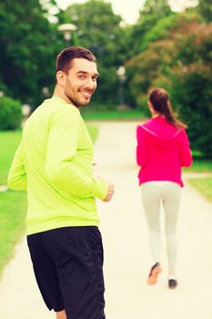 fitness, sport, friendship and lifestyle concept - smiling couple running outdoors