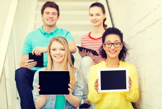 education and technology concept - smiling students showing tablet pc computer blank screen and sitting on staircase