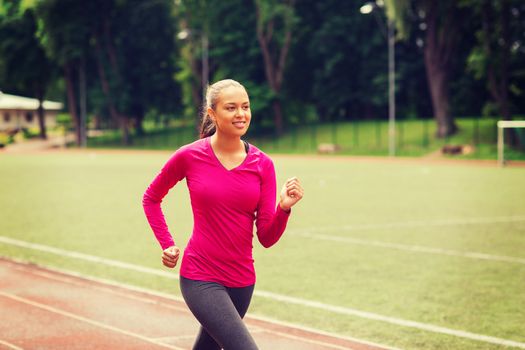 fitness, sport, training and lifestyle concept - smiling african american woman running on track outdoors