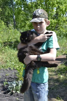 The teenage boy holds on hands of a black fluffy cat.