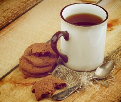 Rustic Cup of Tea with Chocolate Chip Cookies and Silver Spoon on Wooden background. Retro Styled