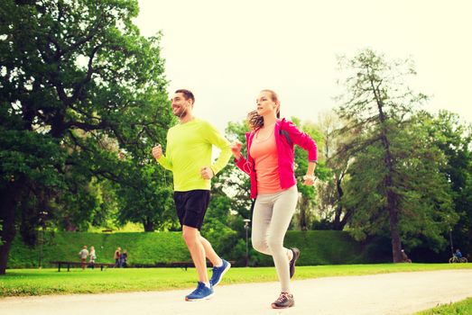 fitness, sport, friendship and lifestyle concept - smiling couple with earphones running outdoors