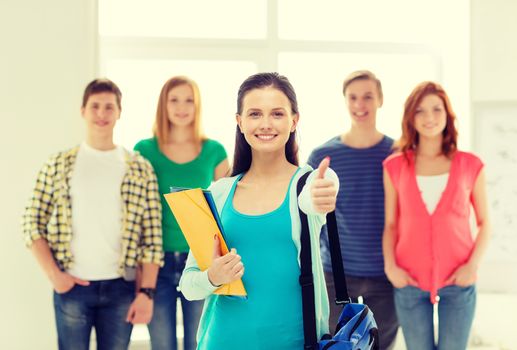 education and school concept - group of smiling students with teenage girl in front with bag and folders showing thumbs up