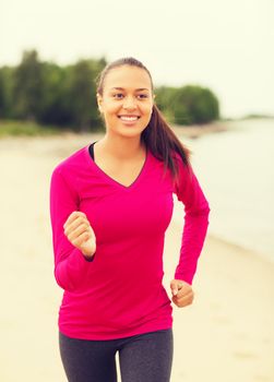 fitness, sport, training and lifestyle concept - smiling african american woman running on track outdoors