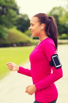 sport, fitness, health, technology and people concept - smiling young african american woman running with smartphone and earphones outdoors