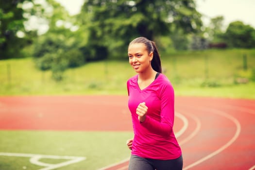 fitness, sport, training and lifestyle concept - smiling african american woman running on track outdoors