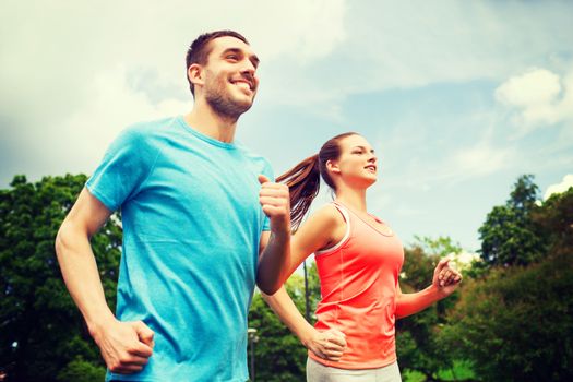 fitness, sport, friendship and lifestyle concept - smiling couple running outdoors