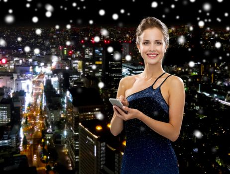 technology, communication and people concept - smiling woman in evening dress holding smartphone over snowy night city background