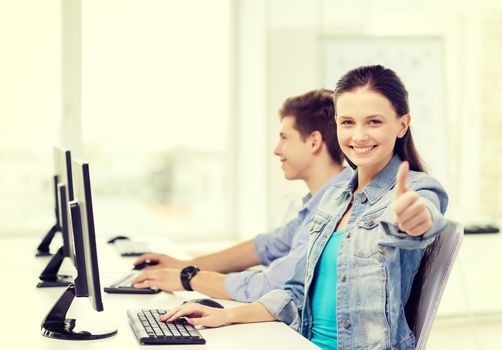 education, gesture, technology and school concept - two smiling students in computer class and girl showing thumbs up