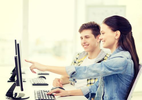 education, technology and school concept - two smiling students in computer class, girl pointing finger at screen