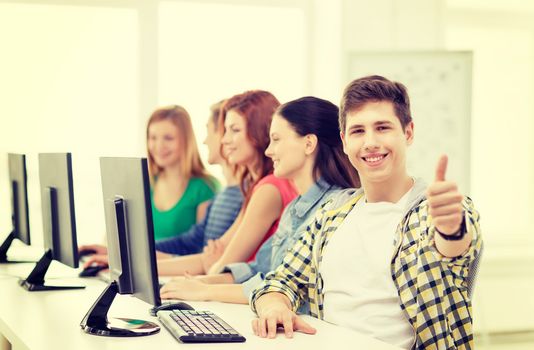 education, technology and school concept - smiling male student with classmates in computer class at school showing thumbs up