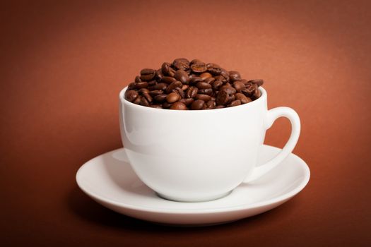 Coffee beans in cup on brown background