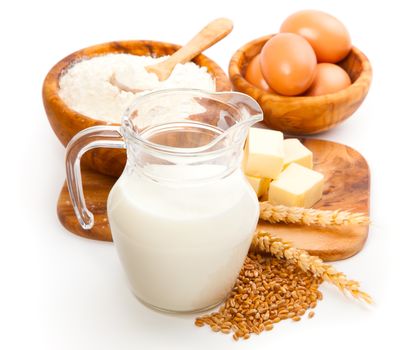 Glass jug with milk, wheat seeds, flour and two eggs on white background