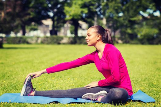 fitness, sport, training, park and lifestyle concept - smiling woman stretching leg on mat outdoors