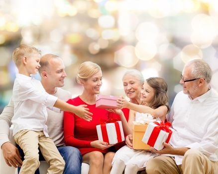 family, holidays, generation, christmas and people concept - smiling family with gift boxes sitting on couch over lights background