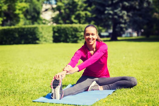 fitness, sport, training, park and lifestyle concept - smiling woman stretching leg on mat outdoors
