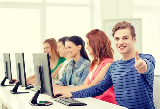 education, technology and school concept - smiling male student with classmates in computer class at school showing thumbs up