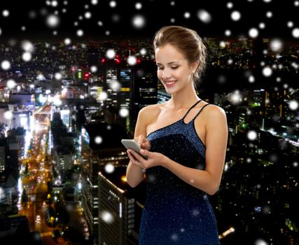 technology, communication and people concept - smiling woman in evening dress holding smartphone over snowy night city background