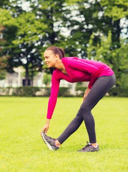 fitness, sport, training, park and lifestyle concept - smiling woman stretching leg outdoors