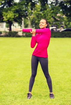 fitness, sport, training, park and lifestyle concept - smiling woman stretching leg outdoors