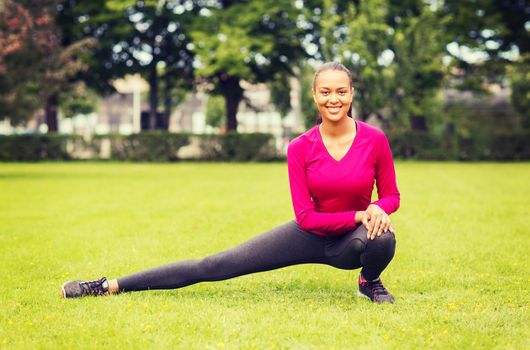 fitness, sport, training, park and lifestyle concept - smiling woman stretching leg outdoors