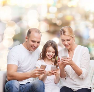 family, holidays, technology and people concept - smiling mother, father and little girl with smartphones over lights background