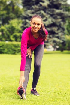 fitness, sport, training, park and lifestyle concept - smiling woman stretching leg outdoors