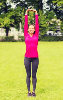 fitness, sport, training, park and lifestyle concept - smiling woman stretching leg outdoors