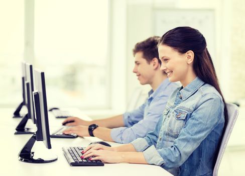 education, technology and school concept - two smiling students in computer class