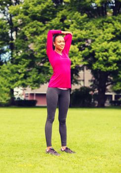 fitness, sport, training, park and lifestyle concept - smiling woman stretching leg outdoors