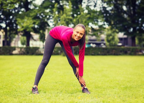 fitness, sport, training, park and lifestyle concept - smiling woman stretching leg outdoors