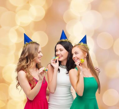 holidays, people and celebration concept - smiling women in party caps blowing to whistles over beige lights background