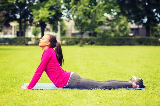 fitness, sport, training, park and lifestyle concept - smiling woman doing exercises on mat outdoors