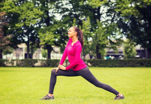 fitness, sport, training, park and lifestyle concept - smiling woman stretching leg outdoors