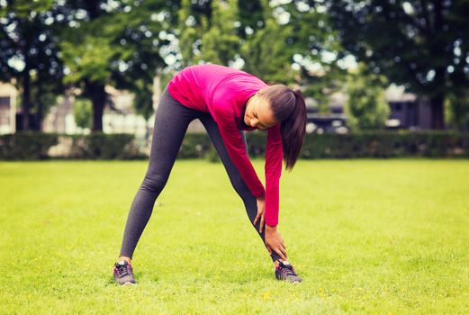 fitness, sport, training, park and lifestyle concept - smiling woman stretching leg outdoors